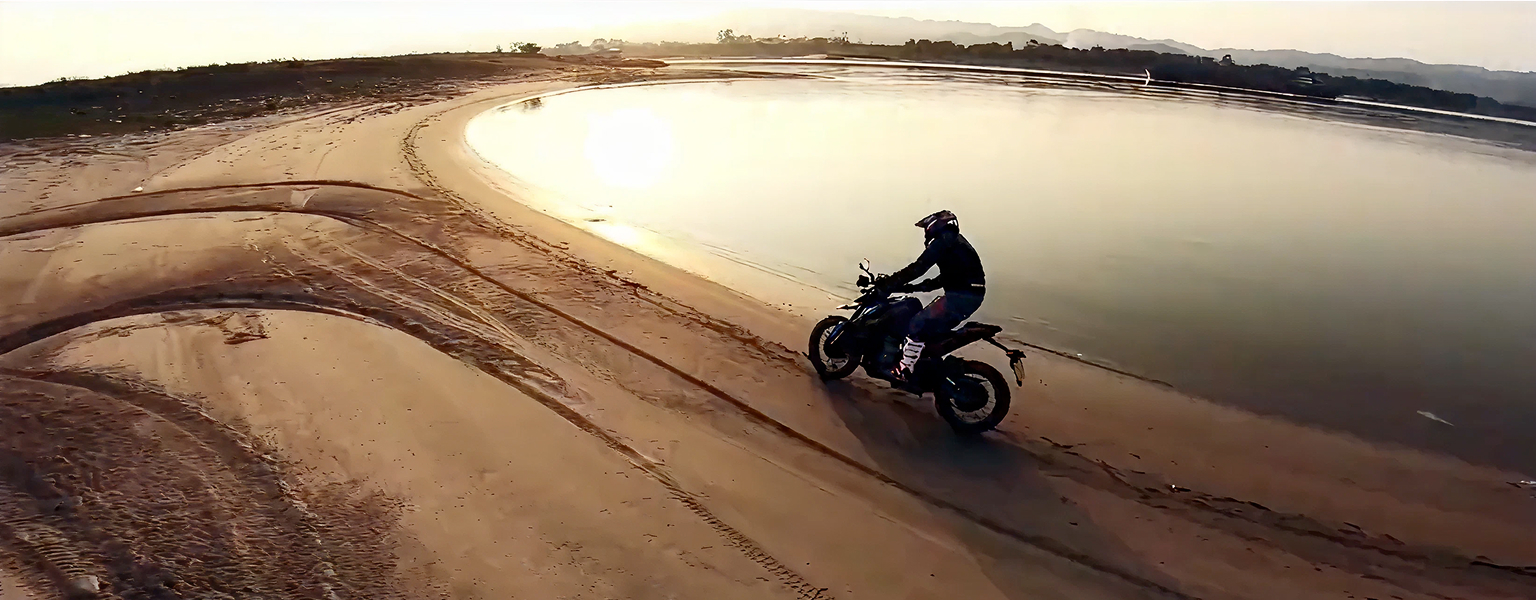 Zontes motos en Uruguay - Zontes 200U circulando sobre arena junto al agua con conductor equipado en una toma amplia.