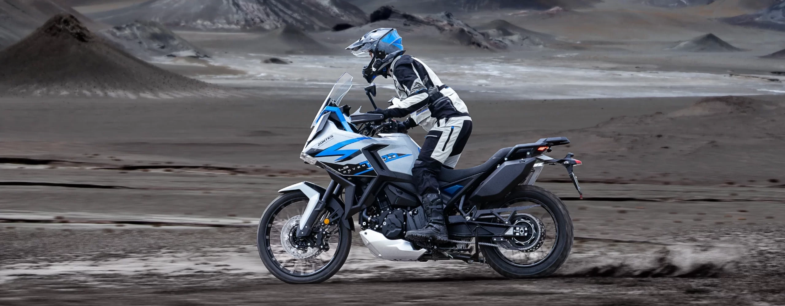 Zontes motos en Uruguay - Moto Zontes 703F rodando en un terreno abierto con piloto de aventura y paisaje amplio al fondo. Zontes motos en Uruguay - Zontes 703F en movimiento sobre suelo oscuro y húmedo con conductor equipado.
