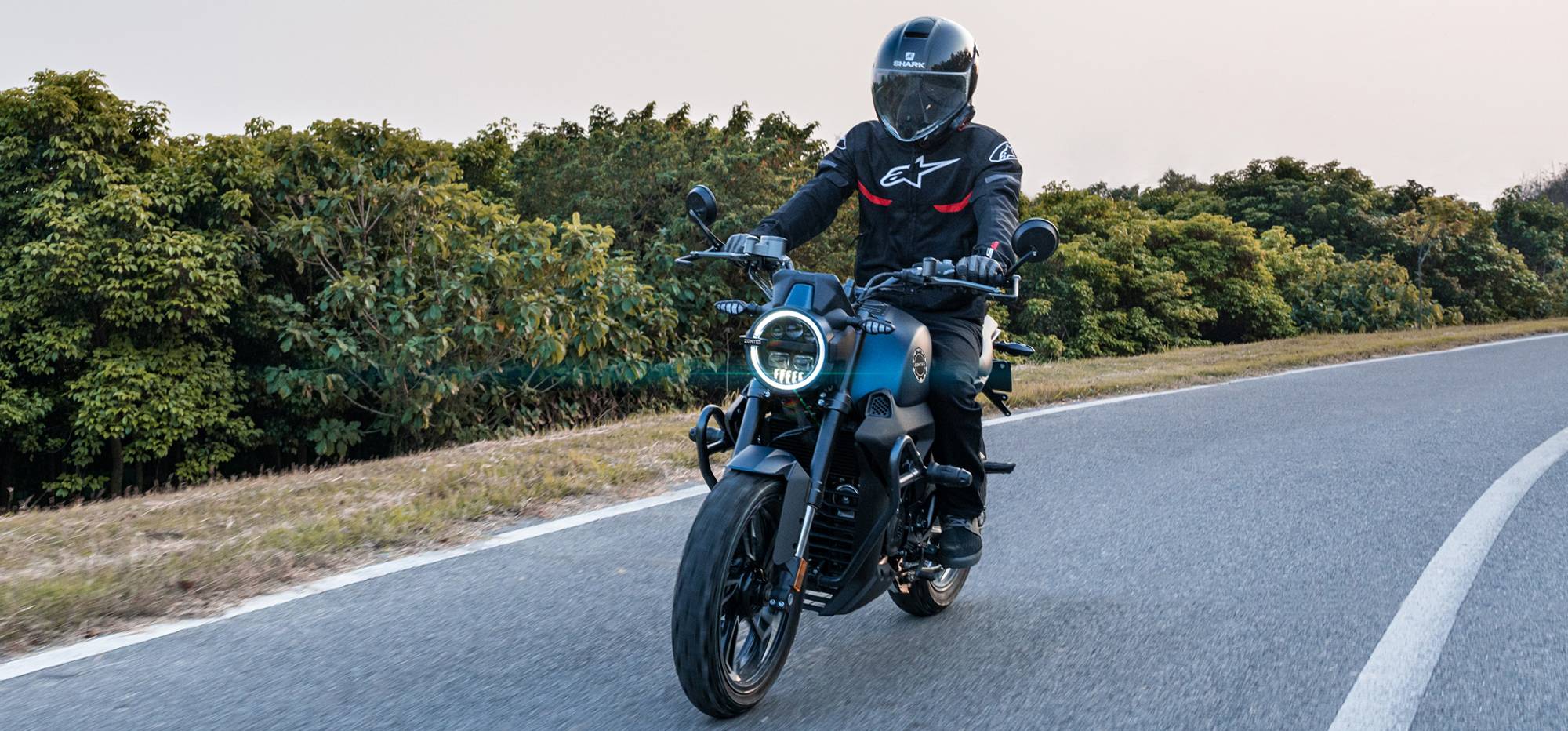Zontes motos en Uruguay - Moto Zontes 200G circulando con piloto de casco integral en una carretera abierta. Zontes motos en Uruguay - Zontes 200G en marcha con conductor equipado sobre una ruta rodeada de vegetación.
