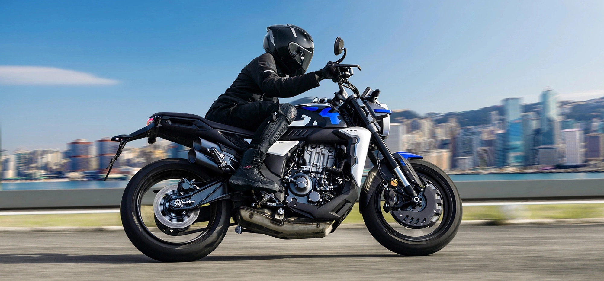 Zontes motos en Uruguay - Moto Zontes 350GK circulando con piloto de casco integral en una escena dinámica urbana. Zontes motos en Uruguay - Zontes 350GK en marcha con conductor equipado y fondo urbano desenfocado.