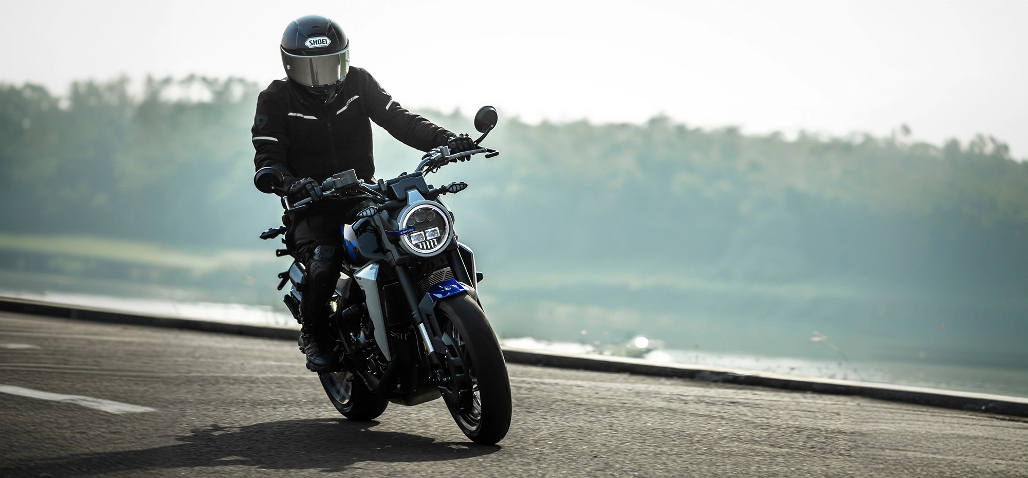 Zontes motos en Uruguay - Moto Zontes 350GK rodando con piloto de casco integral en una escena exterior abierta. Zontes motos en Uruguay - Zontes 350GK en marcha con conductor equipado sobre un camino junto al agua.