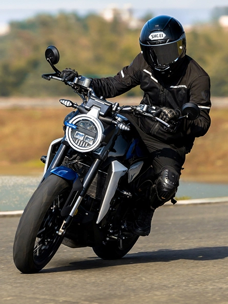 Zontes motos en Uruguay - Zontes 350GK en curva con conductor vestido de negro y faro redondo encendido.