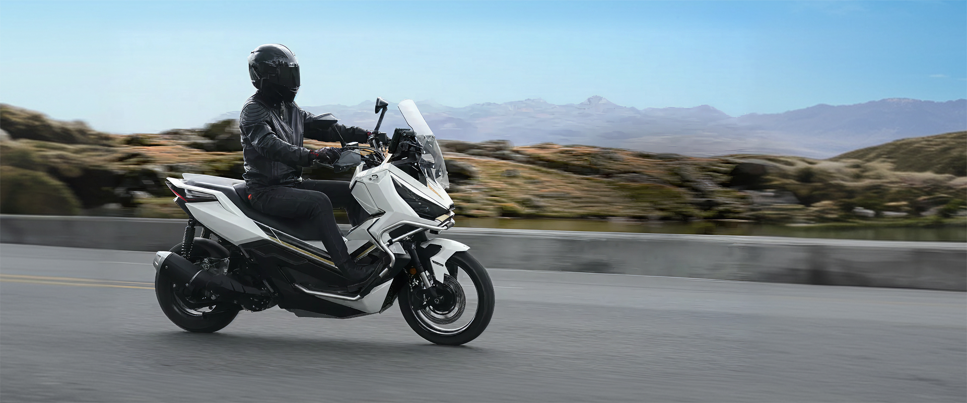 Zontes motos en Uruguay - Scooter Zontes 368G Adventure blanco y negro en marcha sobre la ruta, con conductor equipado y paisaje de montaña al fondo.