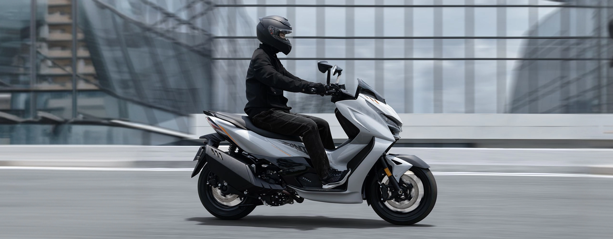 Zontes motos en Uruguay - Scooter 368D circulando en ciudad con conductor, carroceria clara y postura de manejo relajada. Zontes motos en Uruguay - Zontes 368D gris claro en movimiento con conductor equipado sobre una avenida entre edificios modernos.