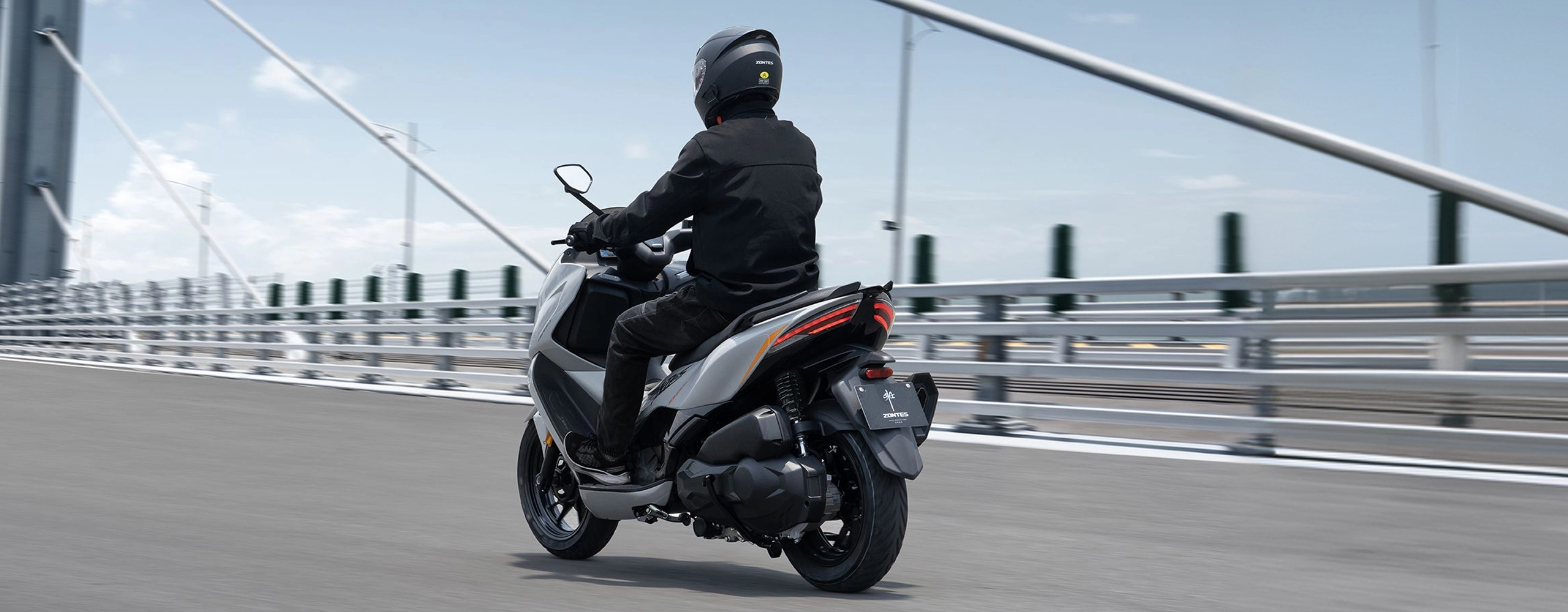 Zontes motos en Uruguay - Scooter 368D circulando con sector trasero visible, suspension lateral y cola estilizada. Zontes motos en Uruguay - Zontes 368D en marcha visto desde atras con conductor y luz posterior encendida sobre un puente urbano.