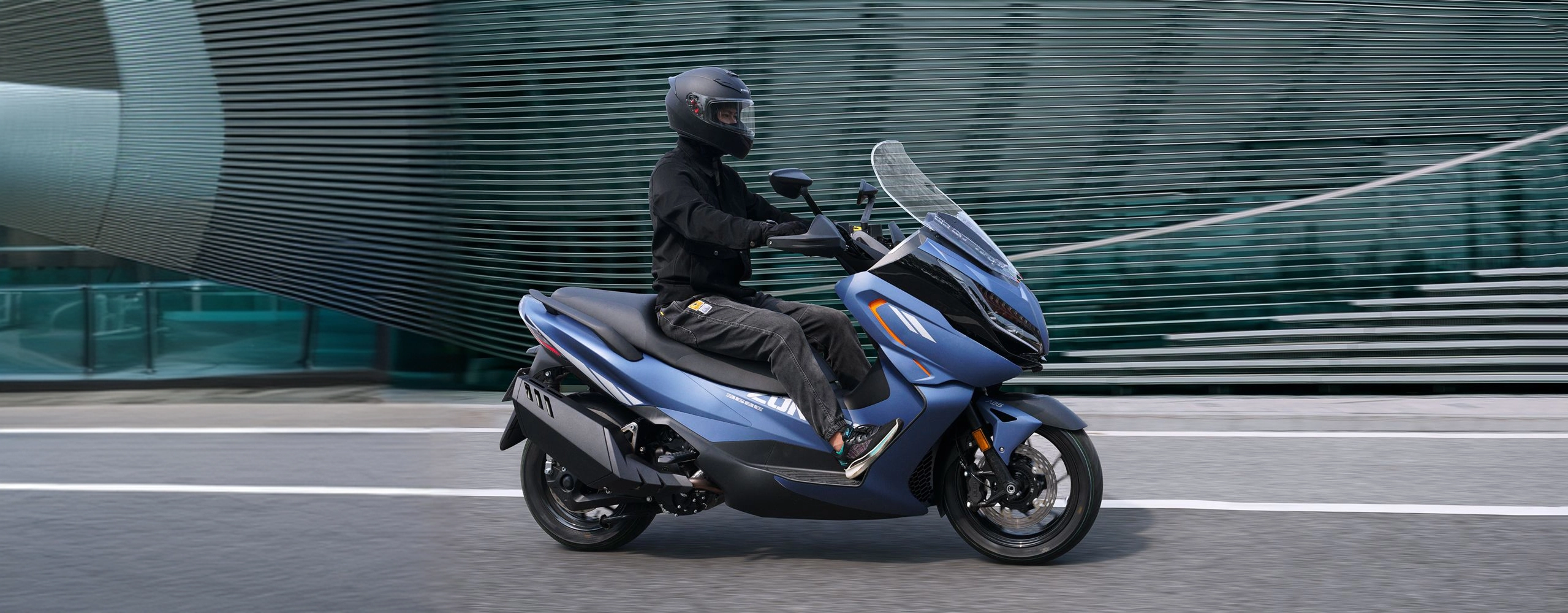 Zontes motos en Uruguay - Zontes 368E azul en movimiento con parabrisas alto y carenado delantero sobre asfalto urbano. Zontes motos en Uruguay - Scooter Zontes 368E azul con conductor circulando por una avenida urbana junto a edificios modernos.