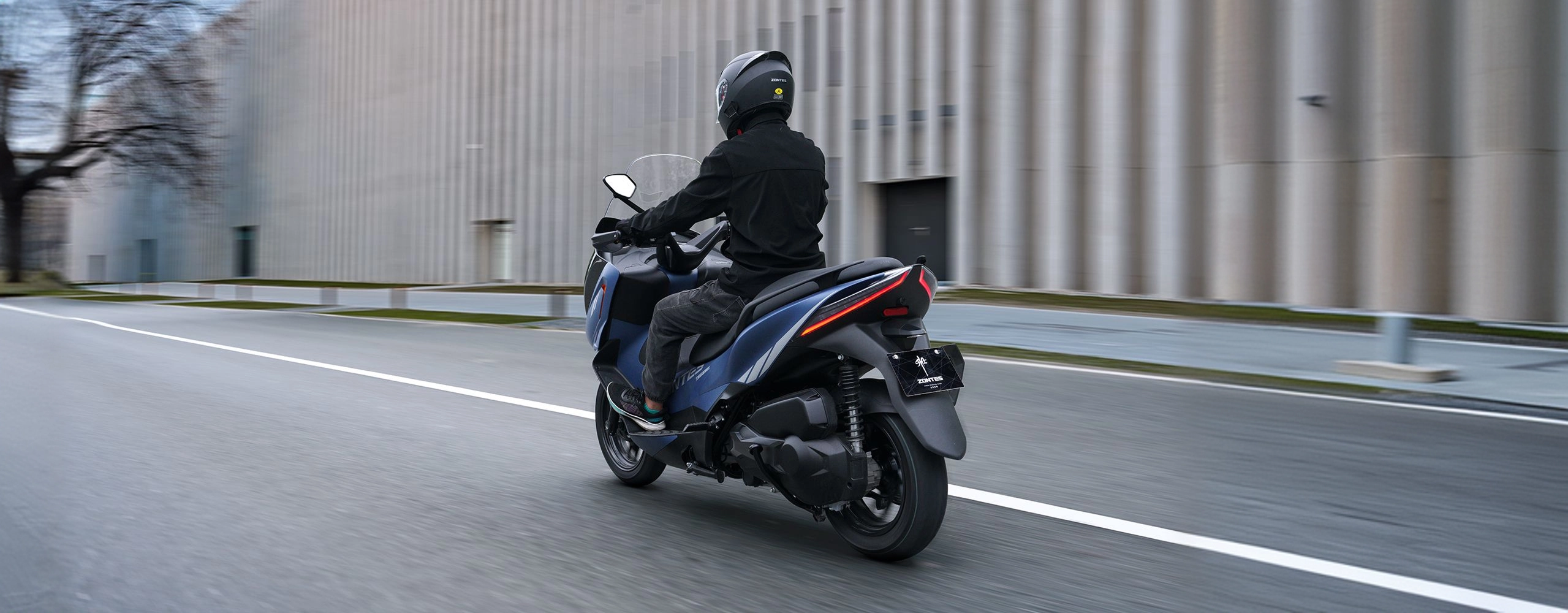 Zontes motos en Uruguay - Scooter 368E azul circulando en ciudad con luz trasera alargada y carroceria posterior estilizada. Zontes motos en Uruguay - Zontes 368E azul en marcha visto desde la parte trasera con conductor sobre una avenida despejada.