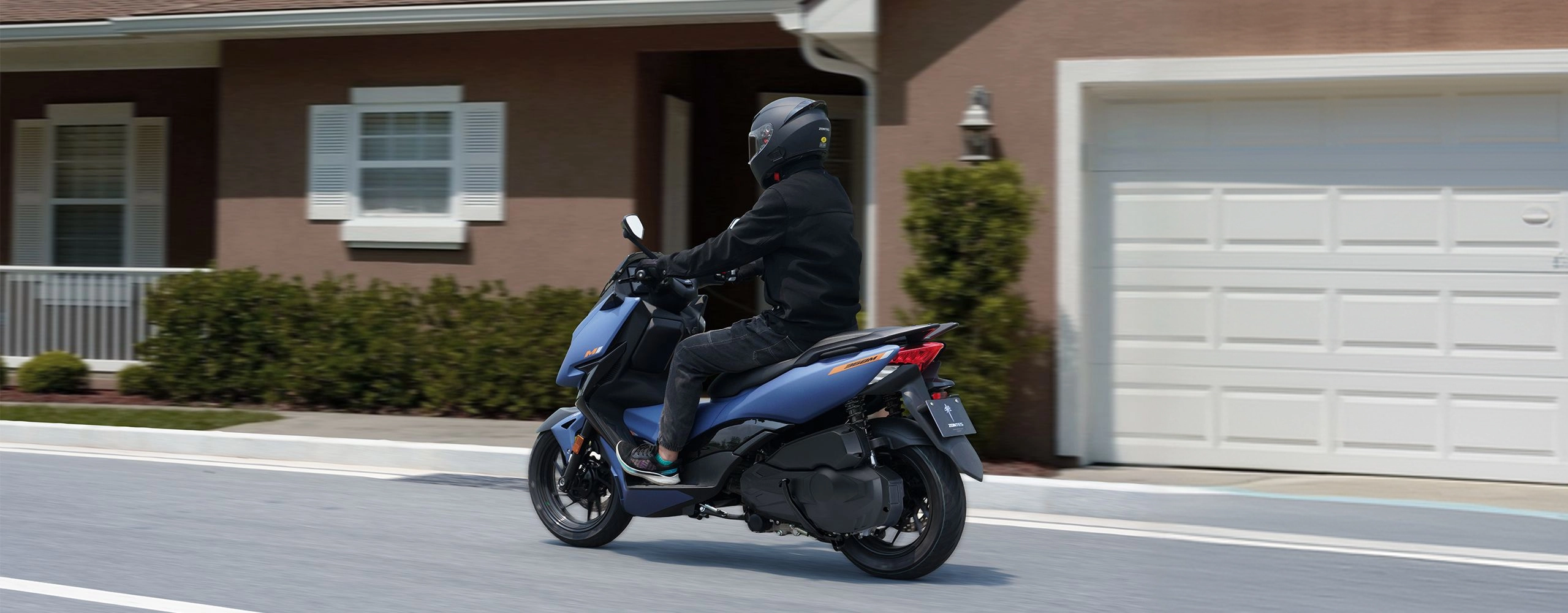Zontes motos en Uruguay - Zontes 368M azul en movimiento frente a viviendas con una postura comoda de manejo. Zontes motos en Uruguay - Scooter Zontes 368M azul con conductor circulando por una calle residencial.