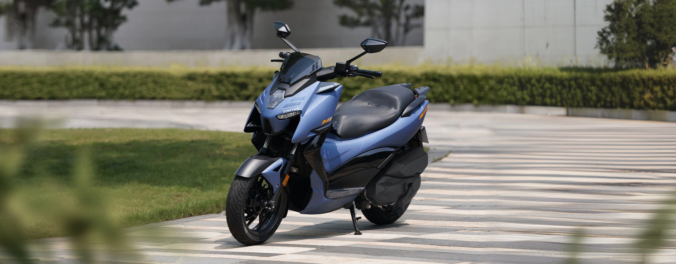 Zontes motos en Uruguay - Zontes 368M azul estacionado con pata lateral desplegada y frente orientado en diagonal. Zontes motos en Uruguay - Scooter Zontes 368M azul detenido sobre una explanada con areas verdes al fondo.